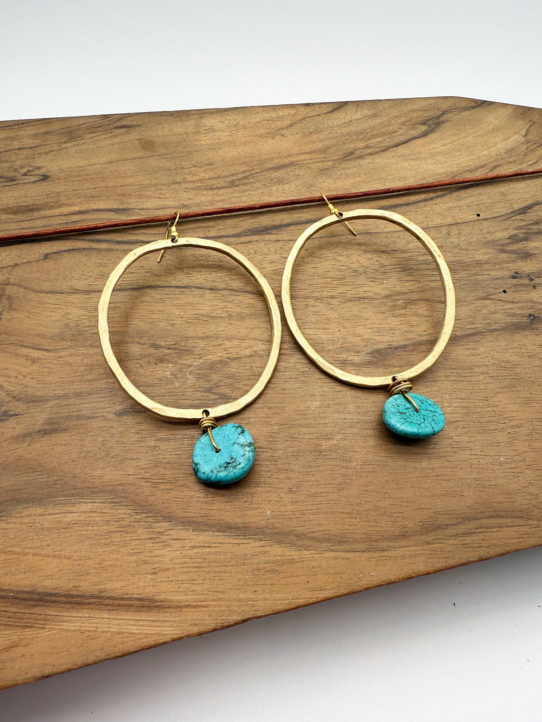 Gold hoop earrings with turquoise charms on a wooden surface