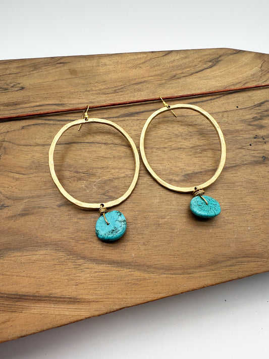 Gold hoop earrings with turquoise charms on a wooden surface
