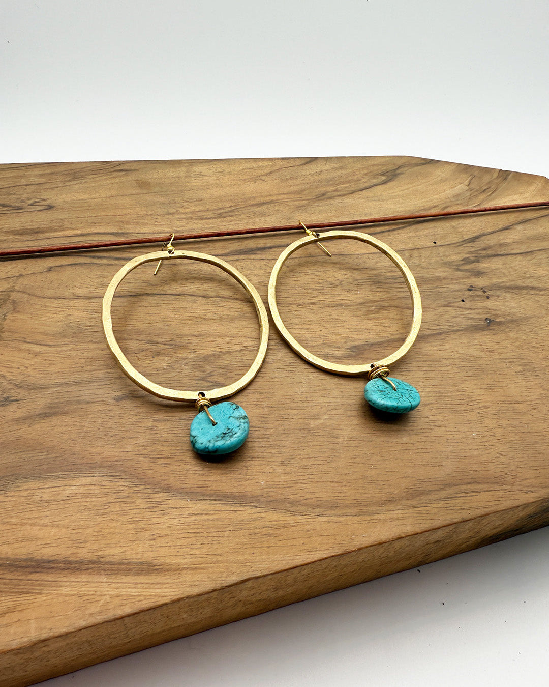 Gold hoop earrings with turquoise stones on a wooden surface