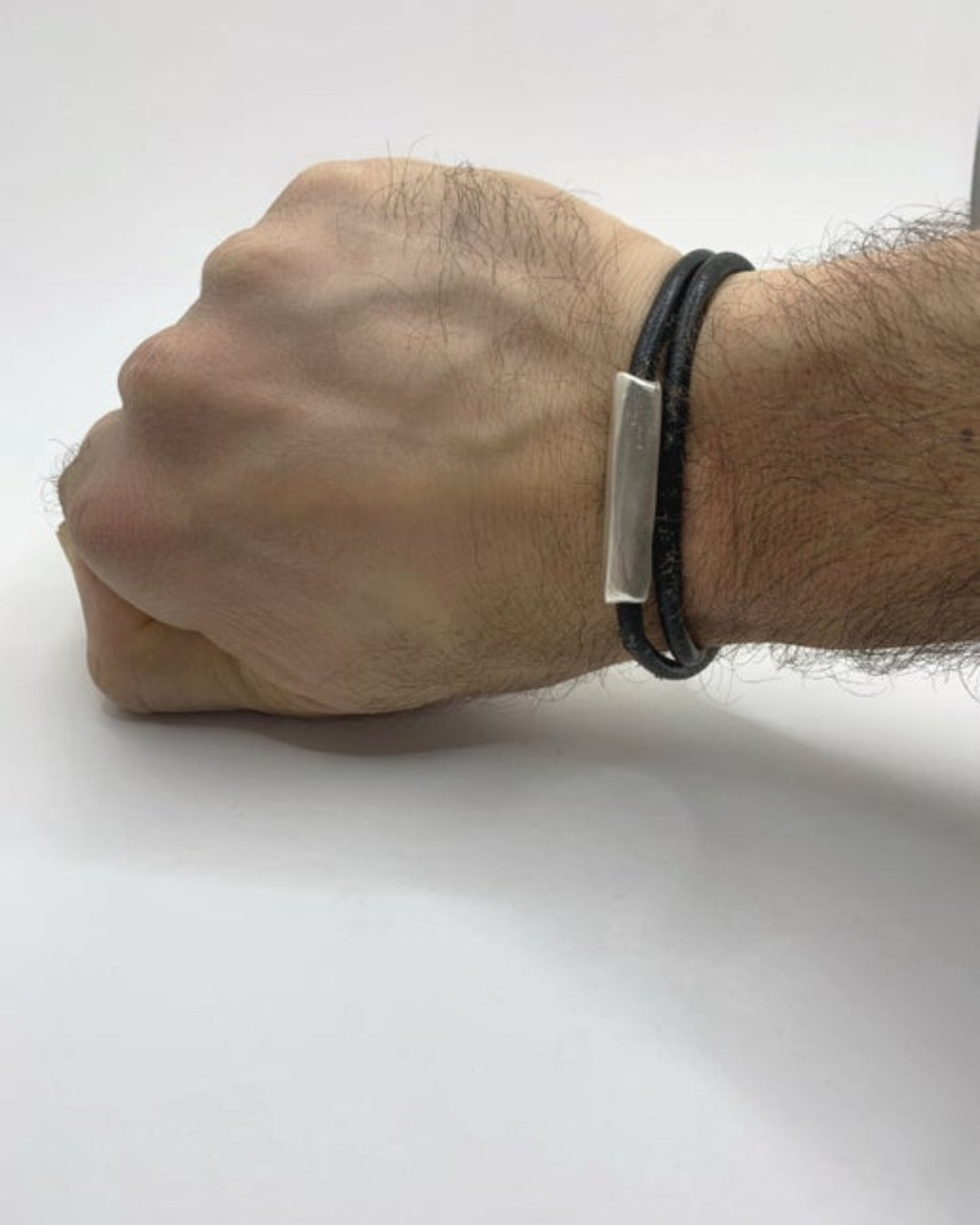 Hand wearing a black double wrap leather bracelet with a silver detail on a white background