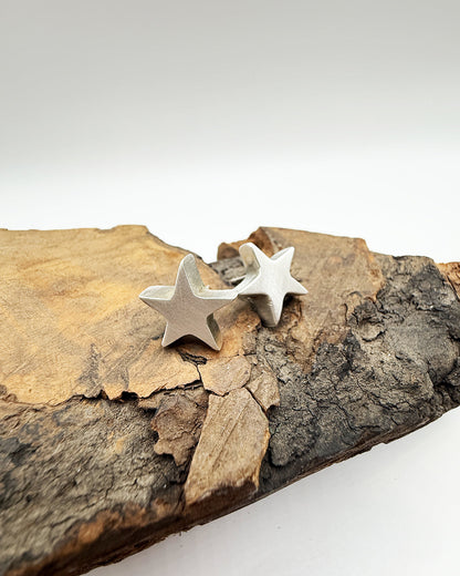 Silver star earrings on a piece of wood with a white background