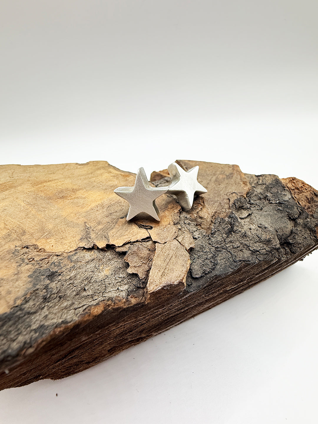 Star-shaped silver earrings on a piece of wood with a white background