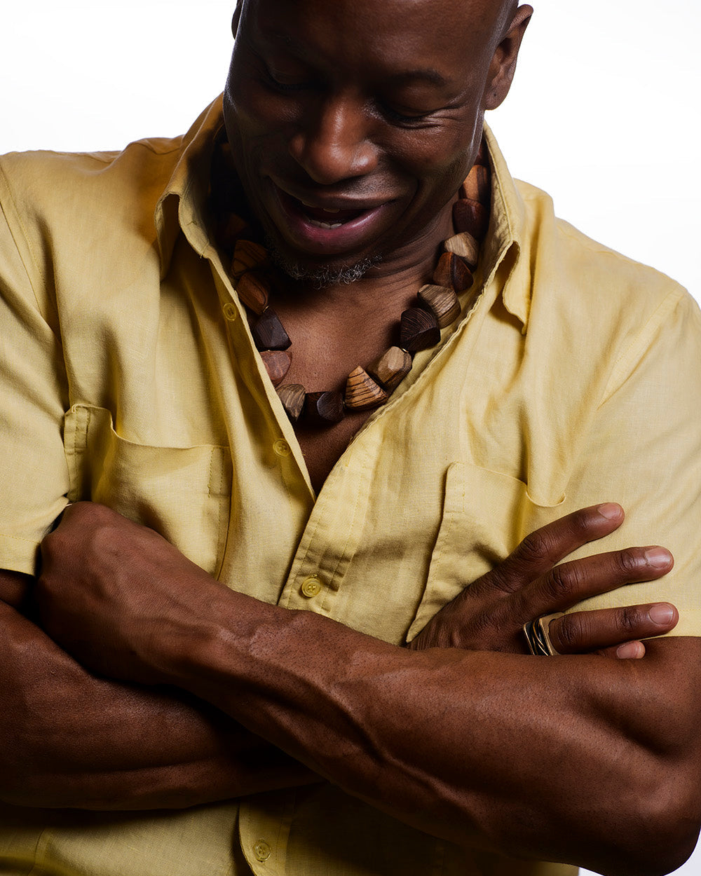 Man wearing a yellow shirt and necklace with arms crossed on a white background