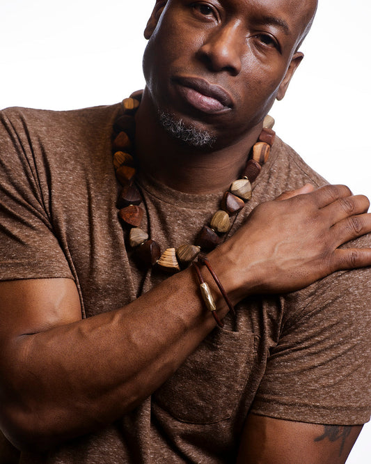 Man wearing a brown shirt with a necklace and bracelets on a white background