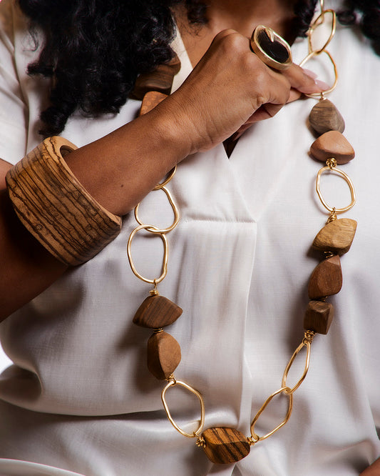 Person wearing a necklace with wooden beads and gold chains on a white background
