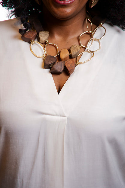 Close-up of a person wearing a necklace with wooden beads and gold accents on a white background