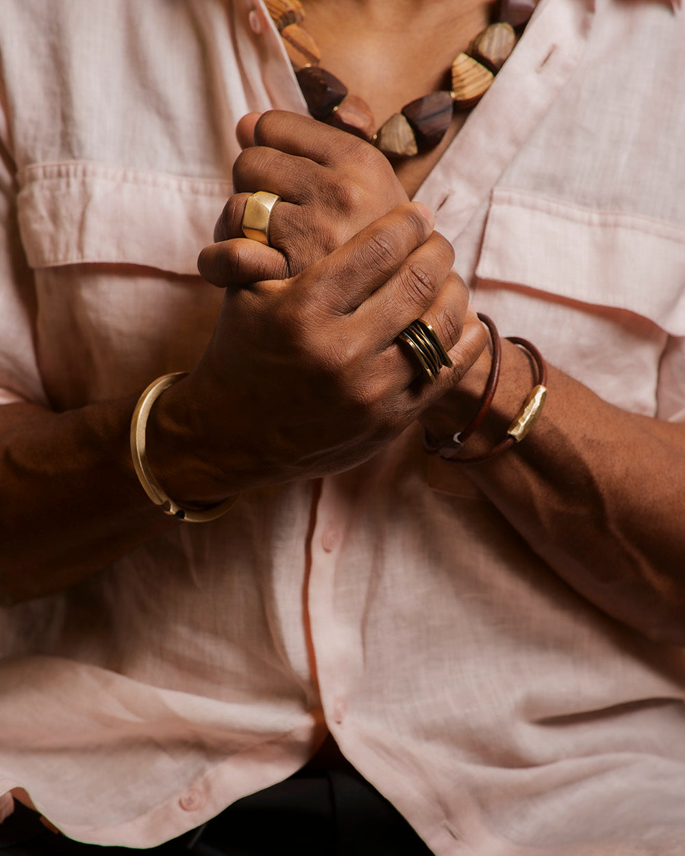 Close-up of a person wearing multiple rings and bracelets on a light shirt background