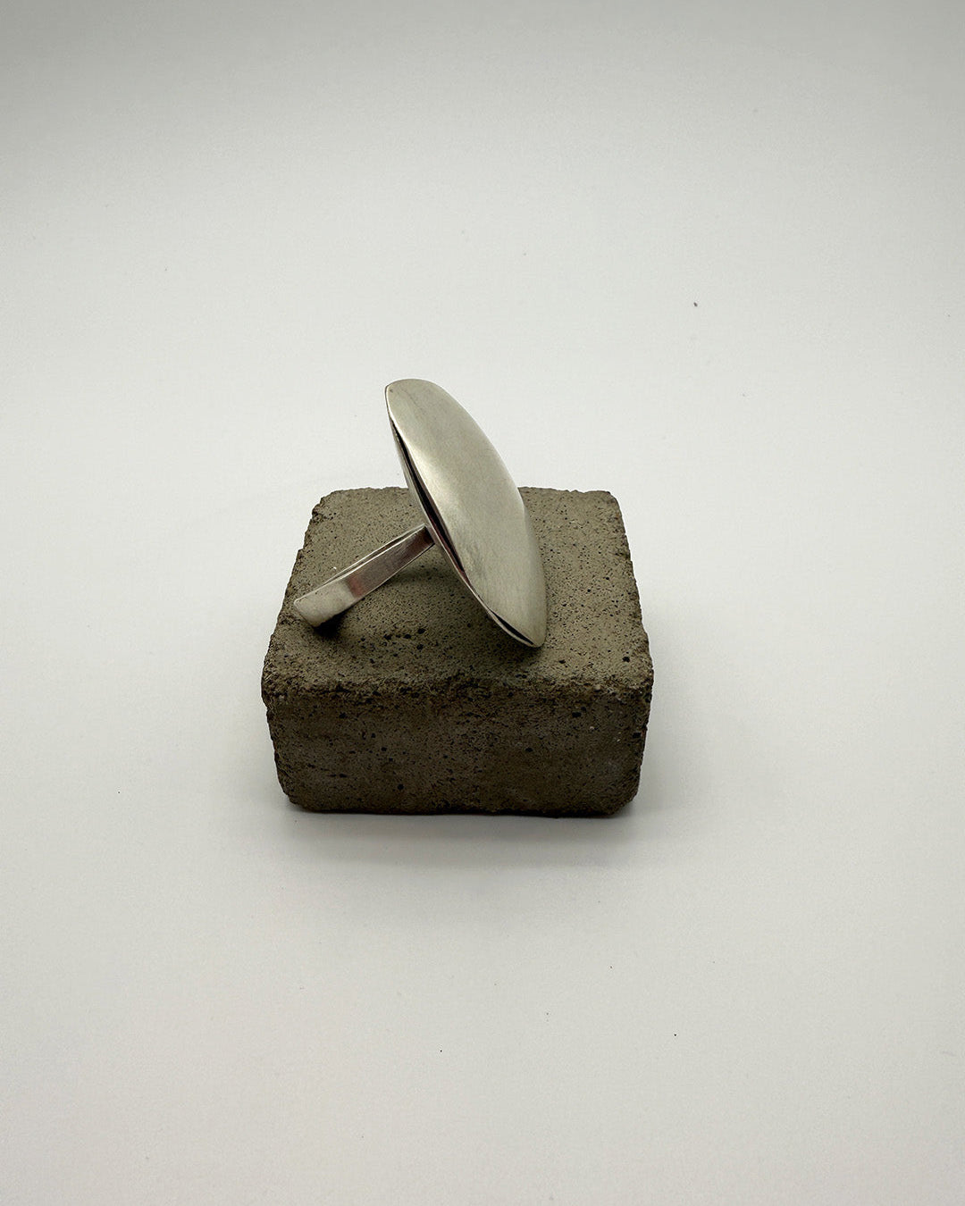 Silver ring on a textured brown block against a white background