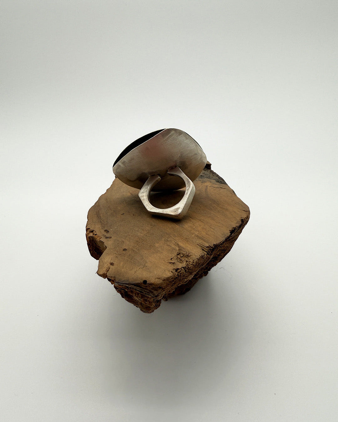 Silver ring on a piece of wood against a white background