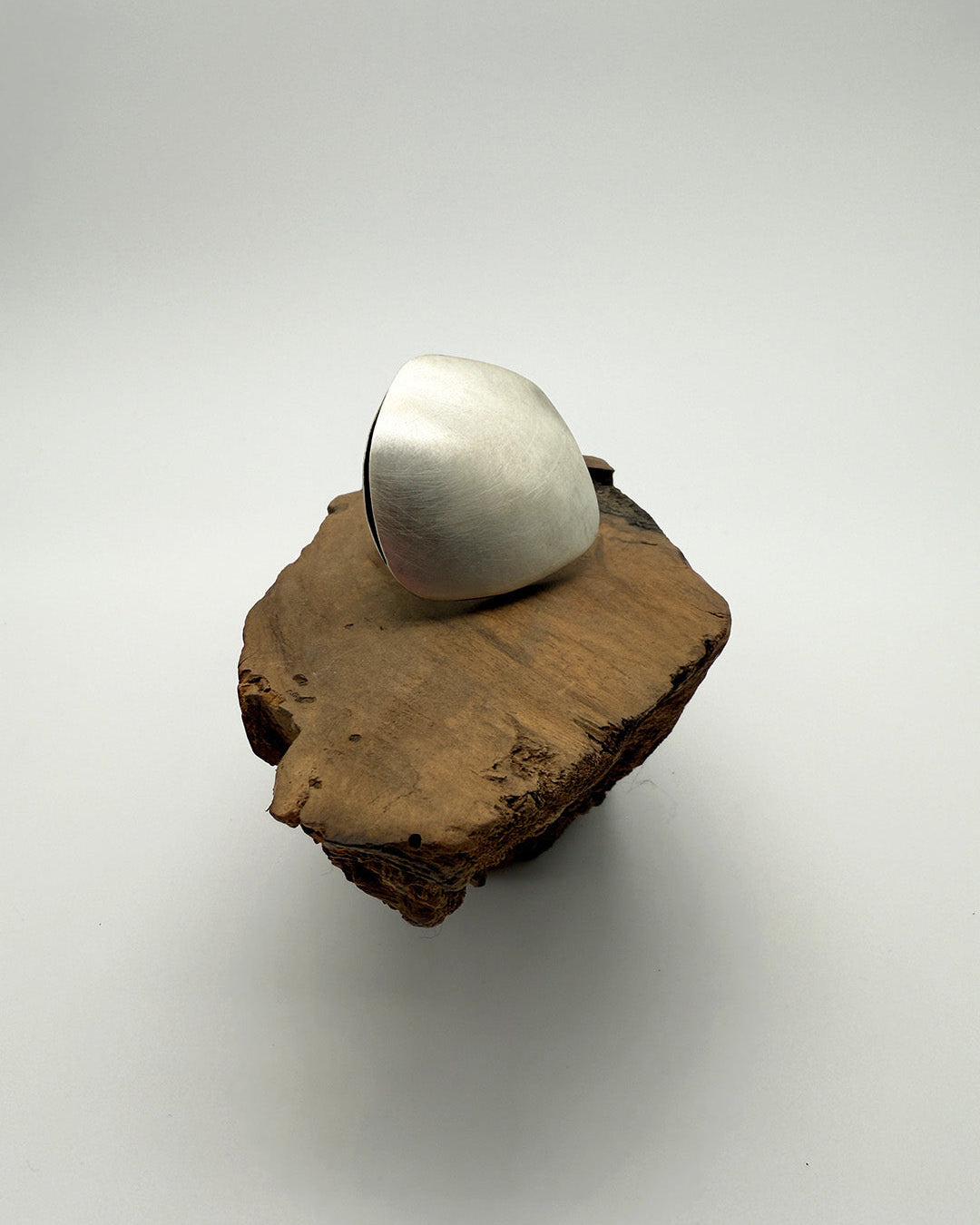 Silver ring on a piece of wood against a white background