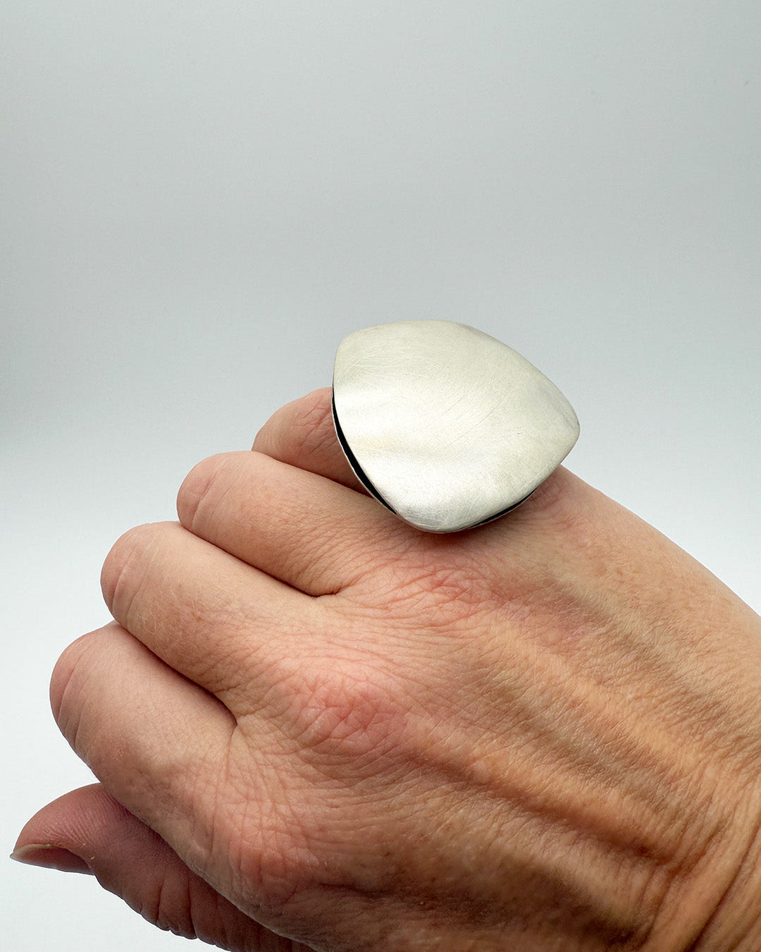 Hand wearing a large silver ring on a plain background