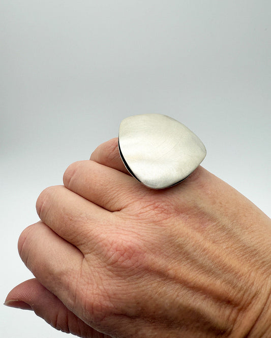 Hand wearing a large silver ring on a plain background