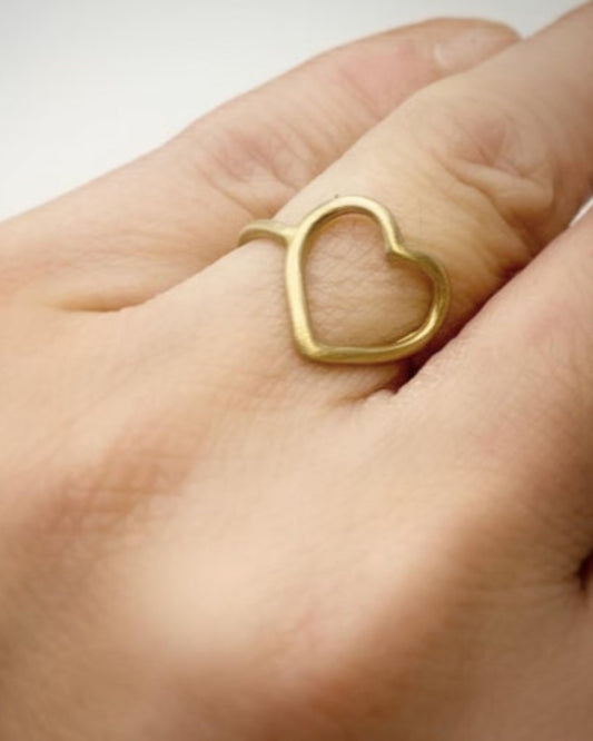 Gold heart-shaped ring on a finger against a neutral background