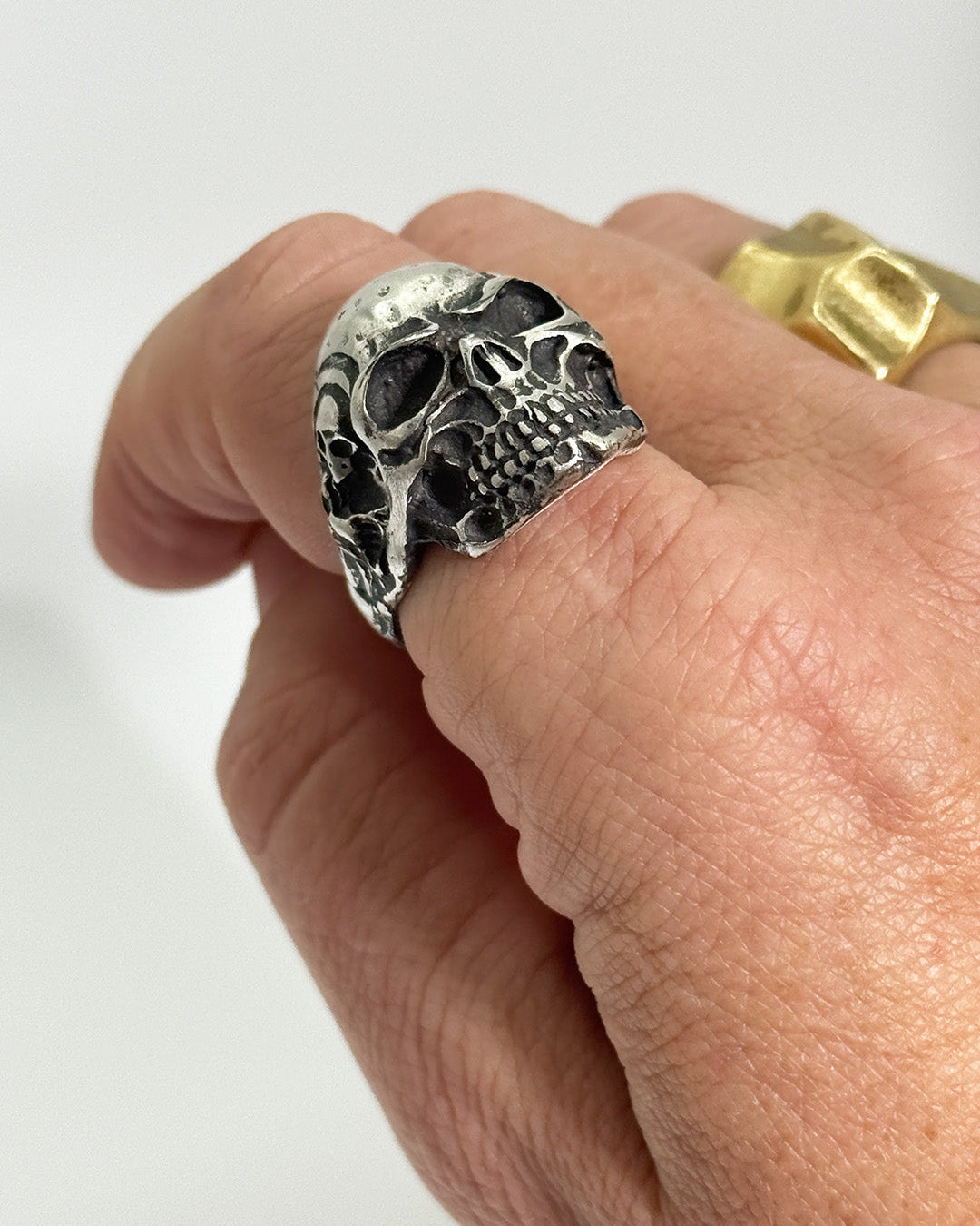 Silver skull ring on a finger against a white background