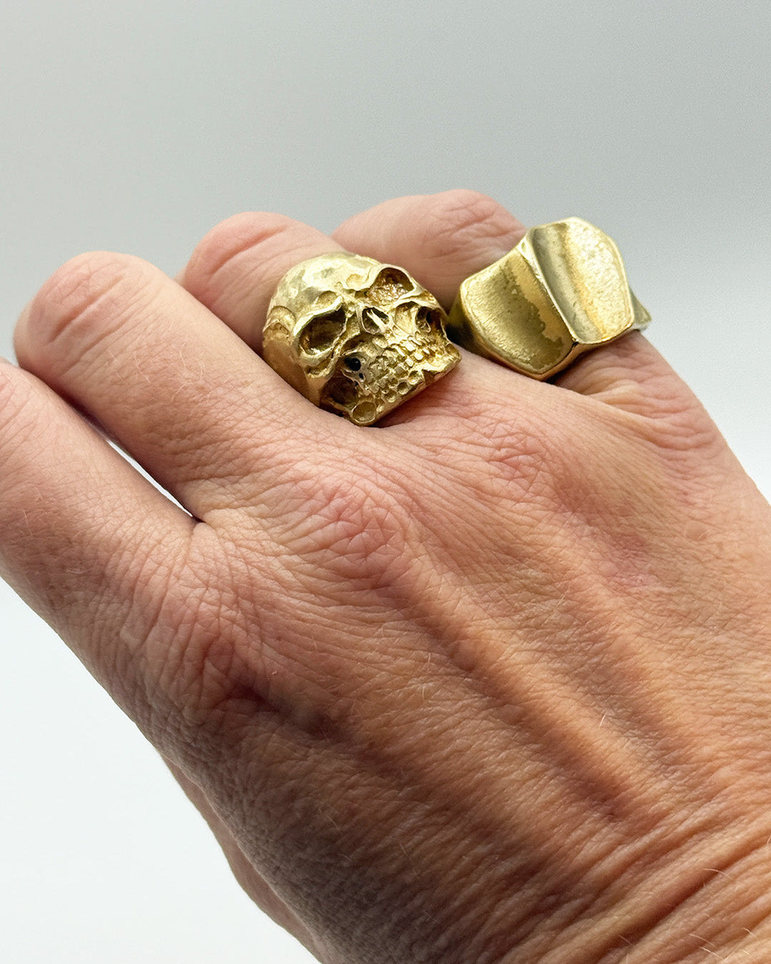 Gold skull ring on a hand with a plain background