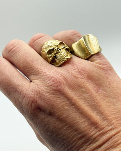 Gold skull ring on a hand with a plain background
