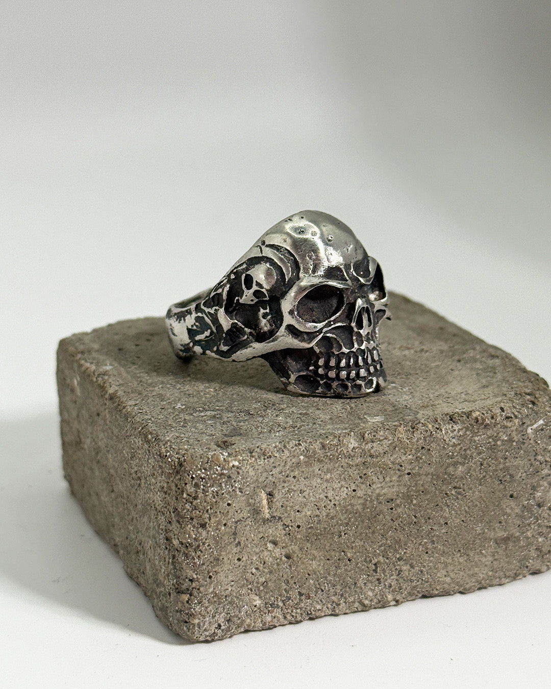 Silver skull ring on a concrete block with a neutral background