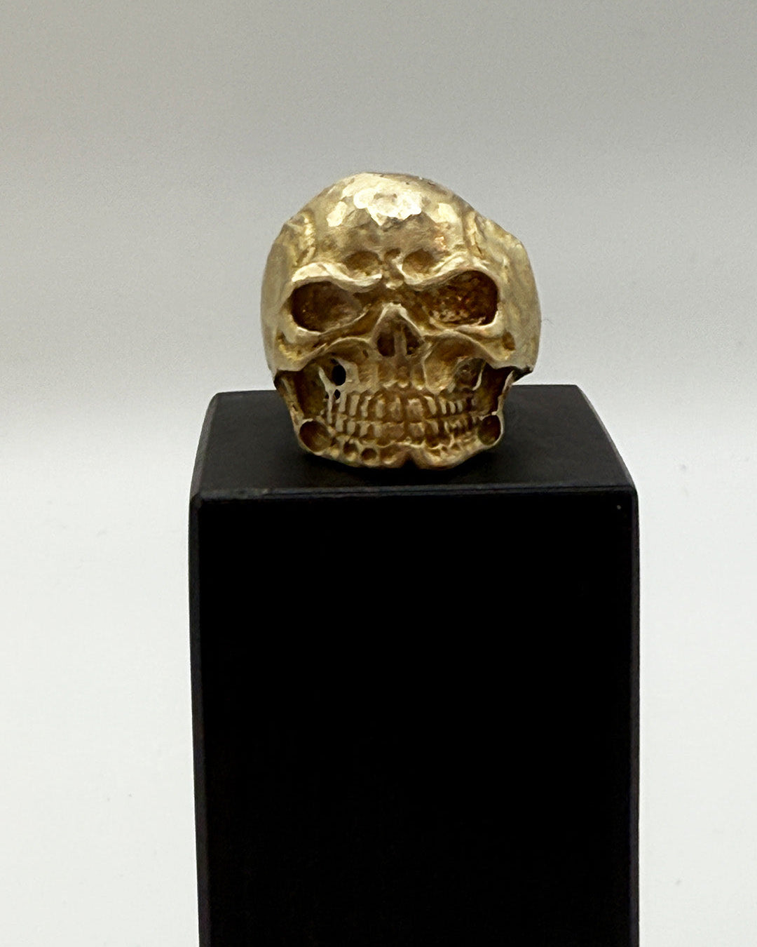 Gold skull figurine on a black pedestal against a gray background