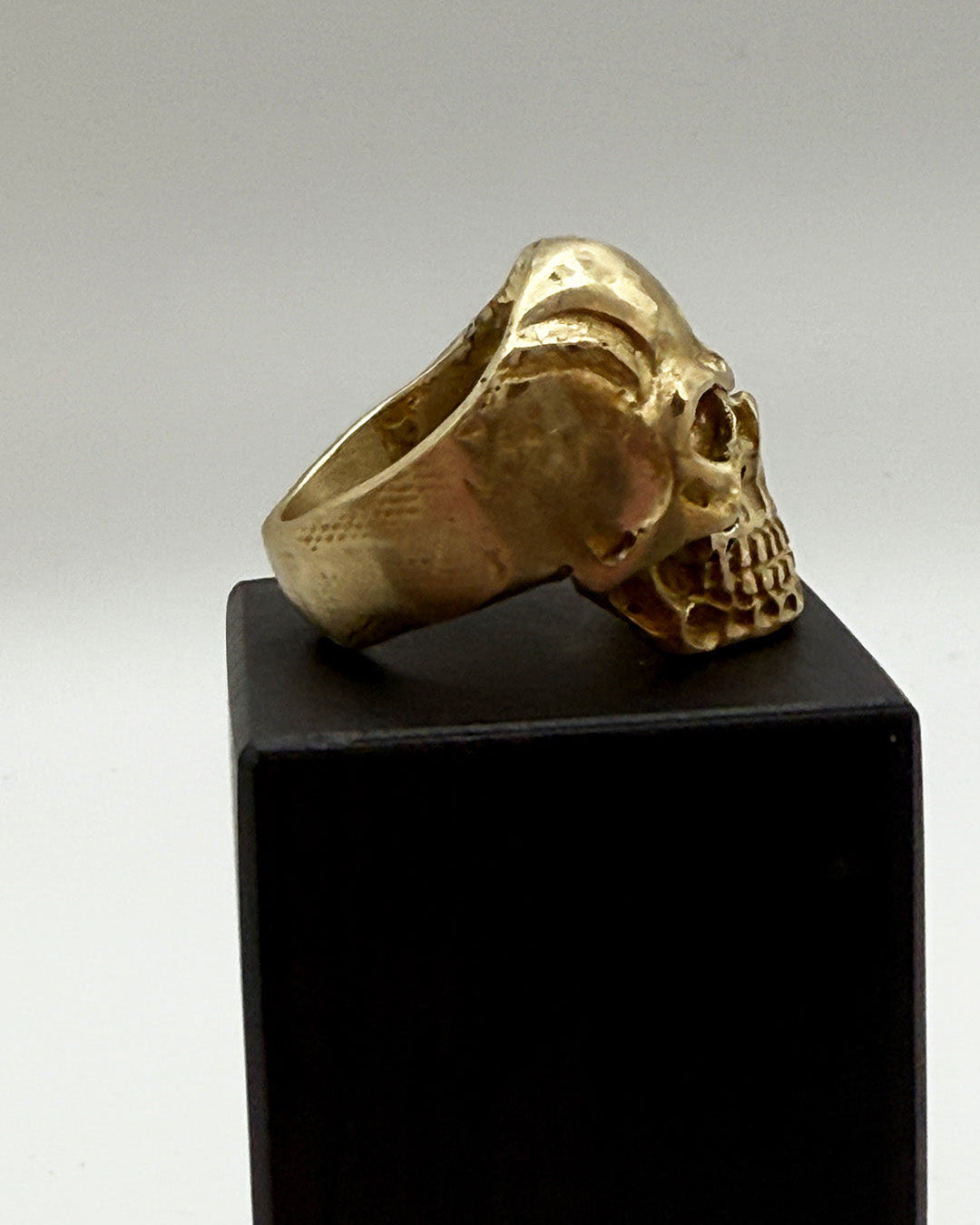 Gold skull ring on a black stand with a gray background