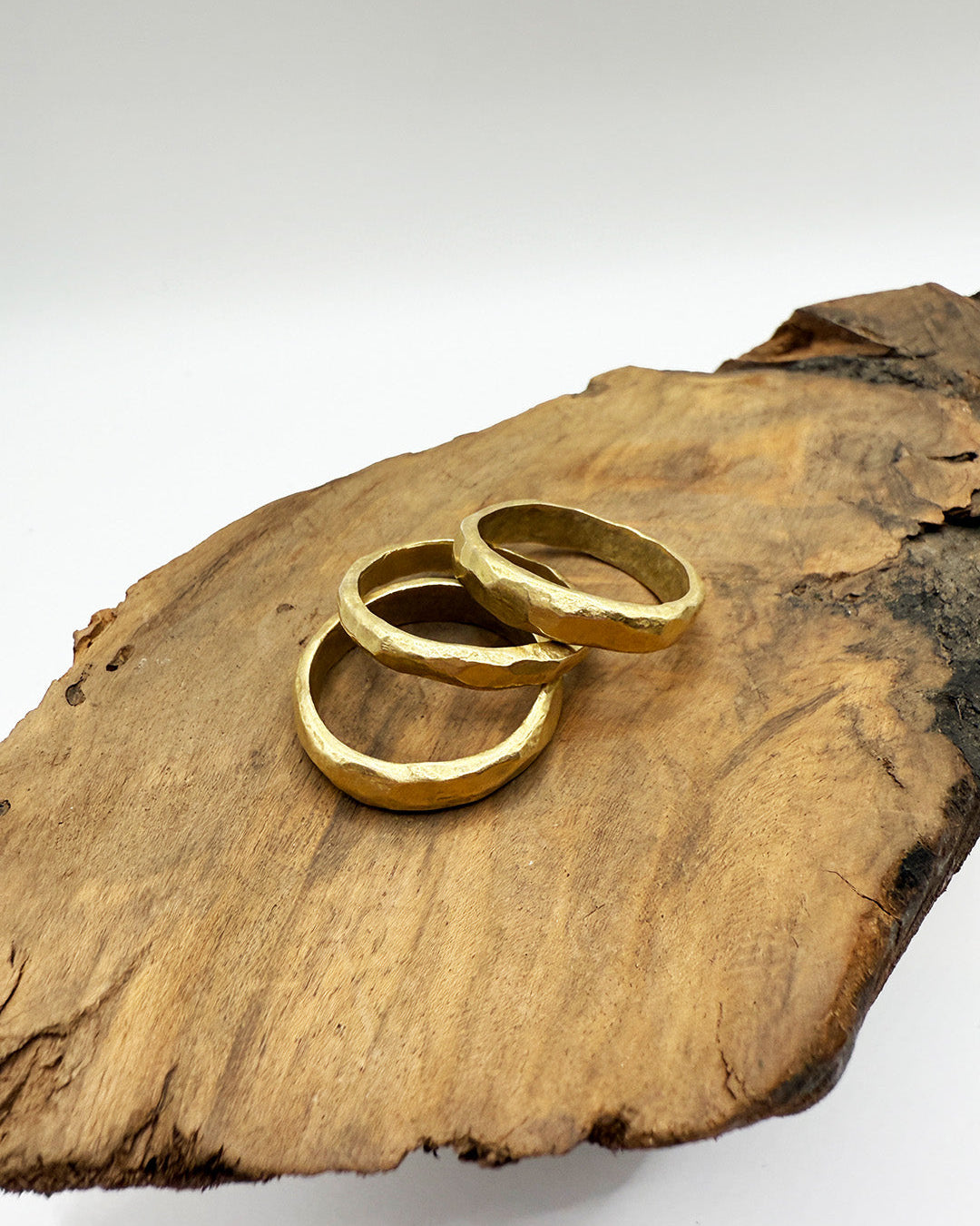 Two gold rings on a wooden surface with a white background
