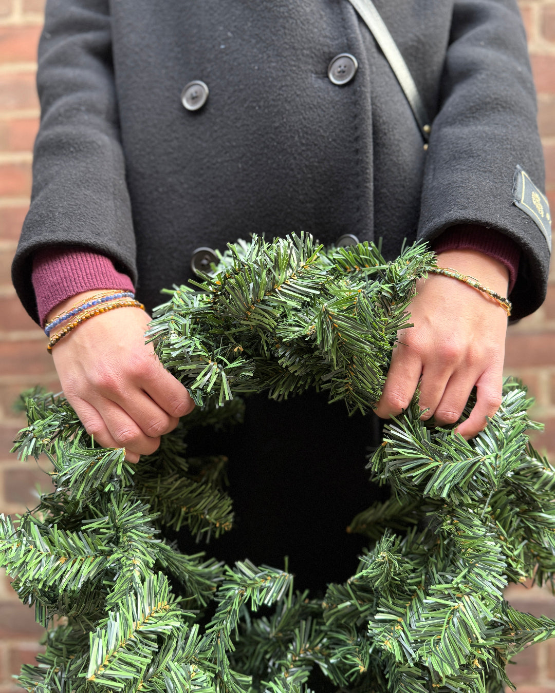 Person holding a green wreath against a brick wall