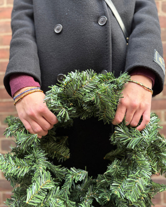 Person holding a green wreath against a brick wall