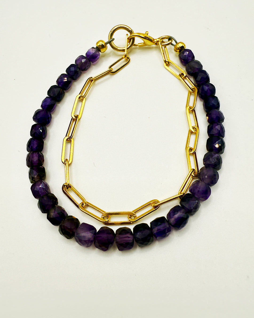 Two purple beaded bracelets with gold chain links on a white background