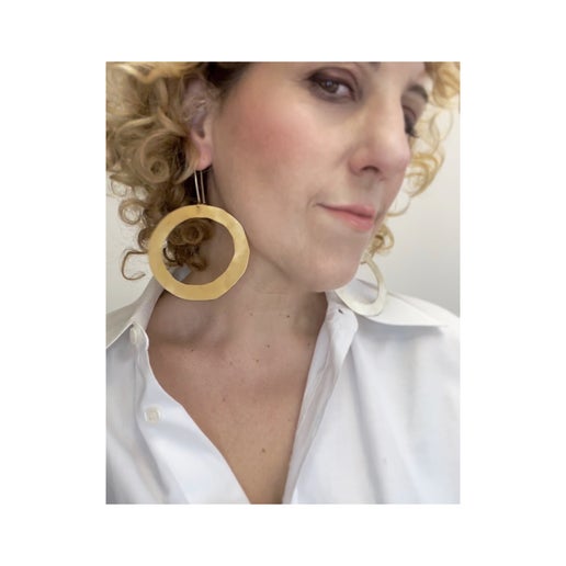Woman wearing large bronze hoop earrings with a white shirt.