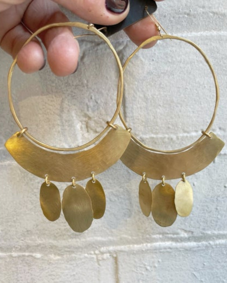 Bronze hoop earrings with hanging oval pendants held against a light background