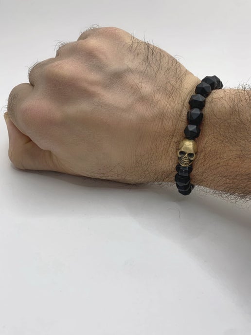 Hand wearing a black beaded bracelet with a skull charm on a white background