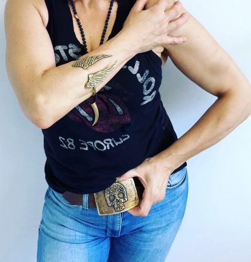 Person wearing a black sleeveless top with graphic design and blue jeans, accessorized with a gold belt buckle.