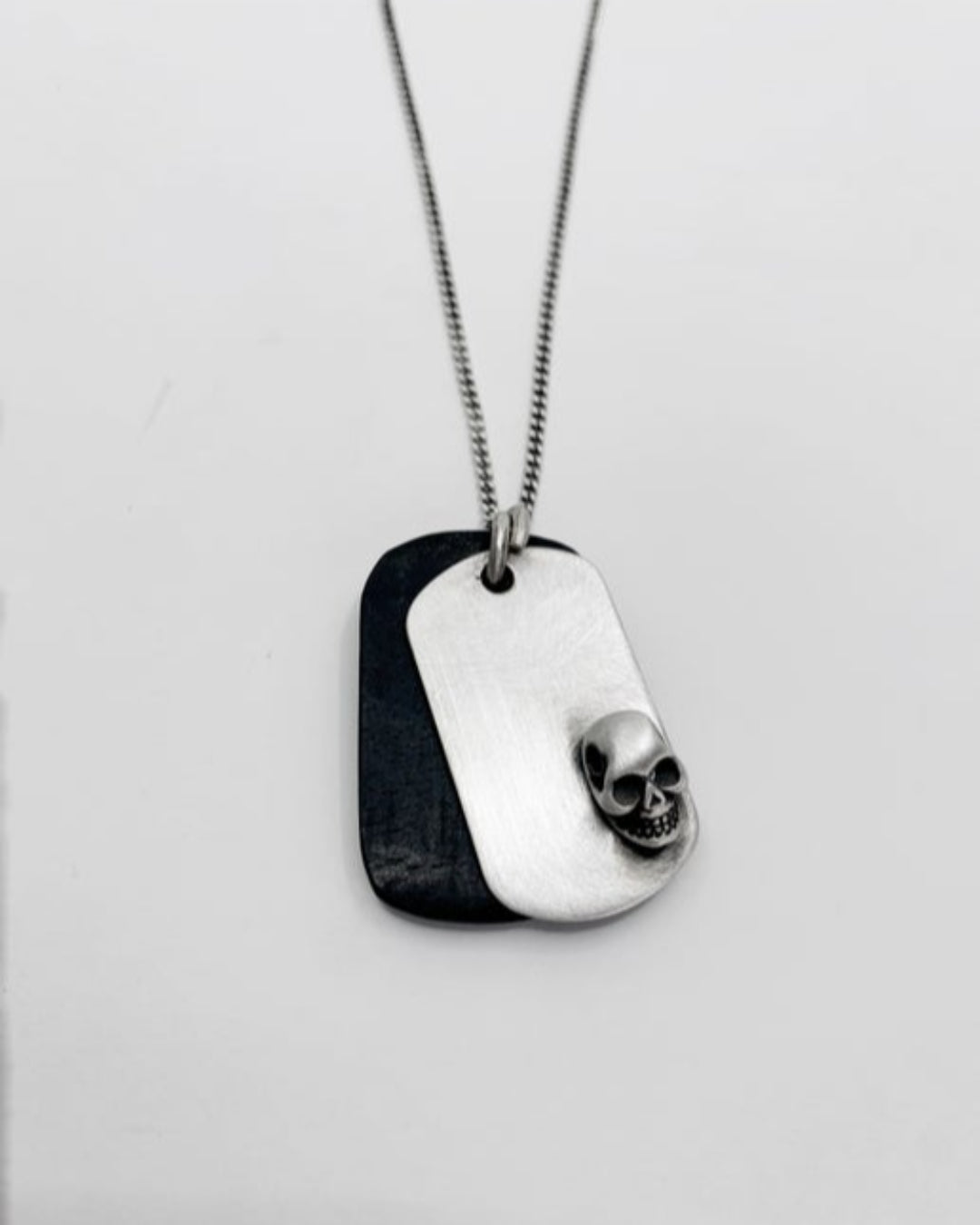 Silver dog tag necklace with a skull design on a light gray background