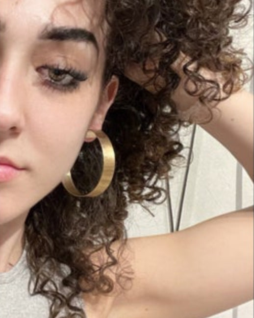 Woman wearing gold hoop earrings with a neutral background