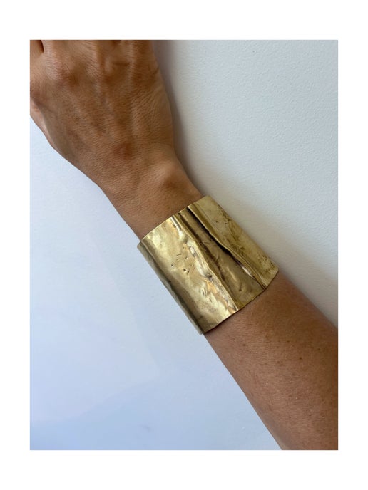 Gold bracelet on a wrist against a light blue background