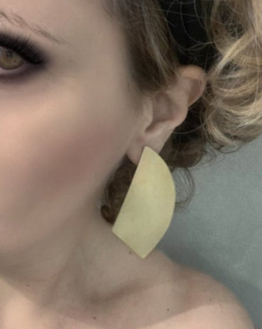 Close-up of a person wearing a large geometric bronze earring with a neutral background