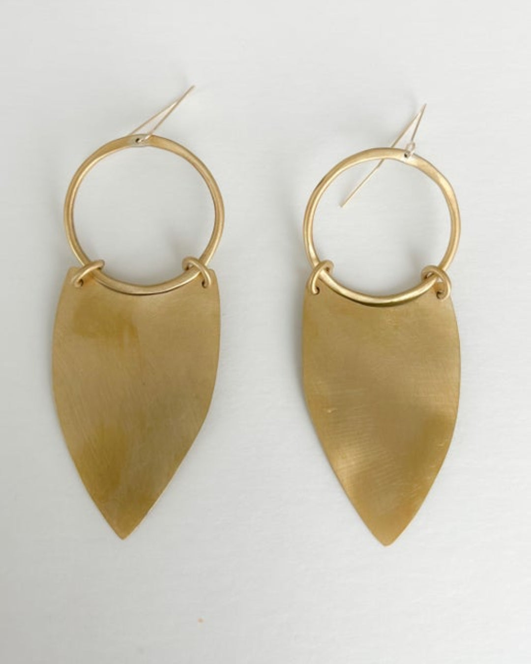 Gold hoop earrings with leaf-shaped pendants on a light gray background