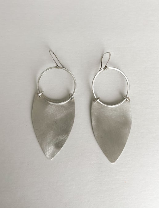 Pair of silver hoop earrings with leaf-shaped pendants on a light gray background