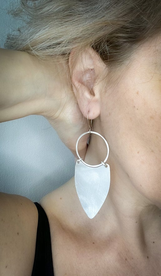 Close-up of a person wearing a silver hoop earring with a leaf shaped pendant