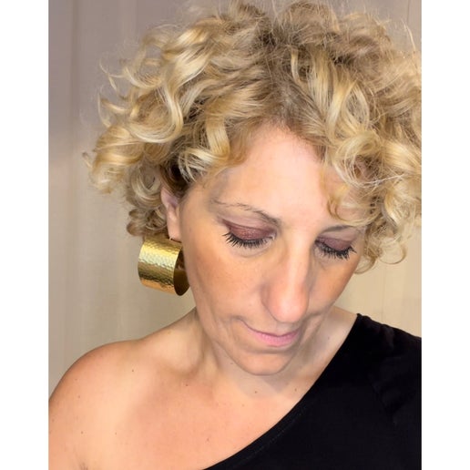 Woman with curly blonde hair wearing gold hoop earrings against a plain background