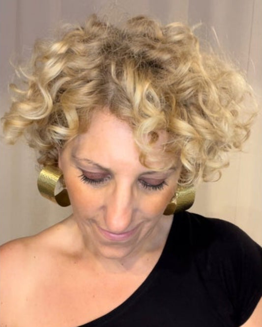Woman with curly blonde hair wearing chunky bronze hoop earrings and  wearing aa black top.