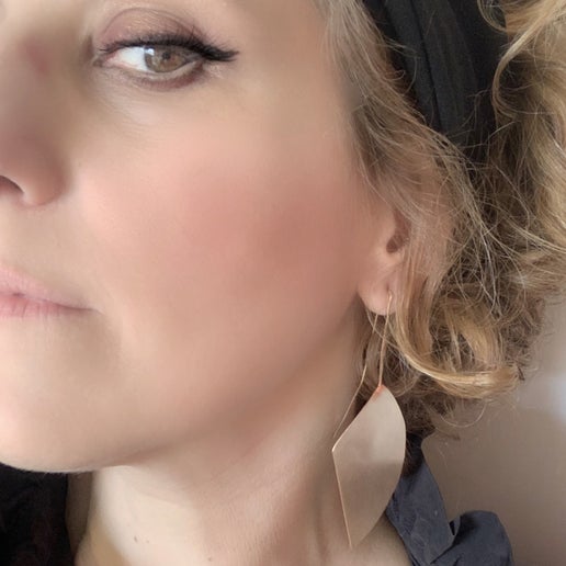 Close-up of a woman wearing a bronze leaf shaped earring with a neutral background