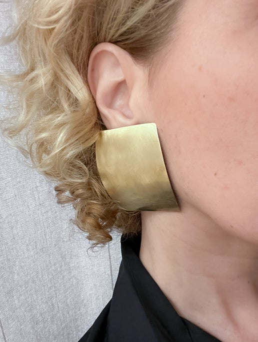 Curved rectangular gold earring worn by a person with blonde hair.