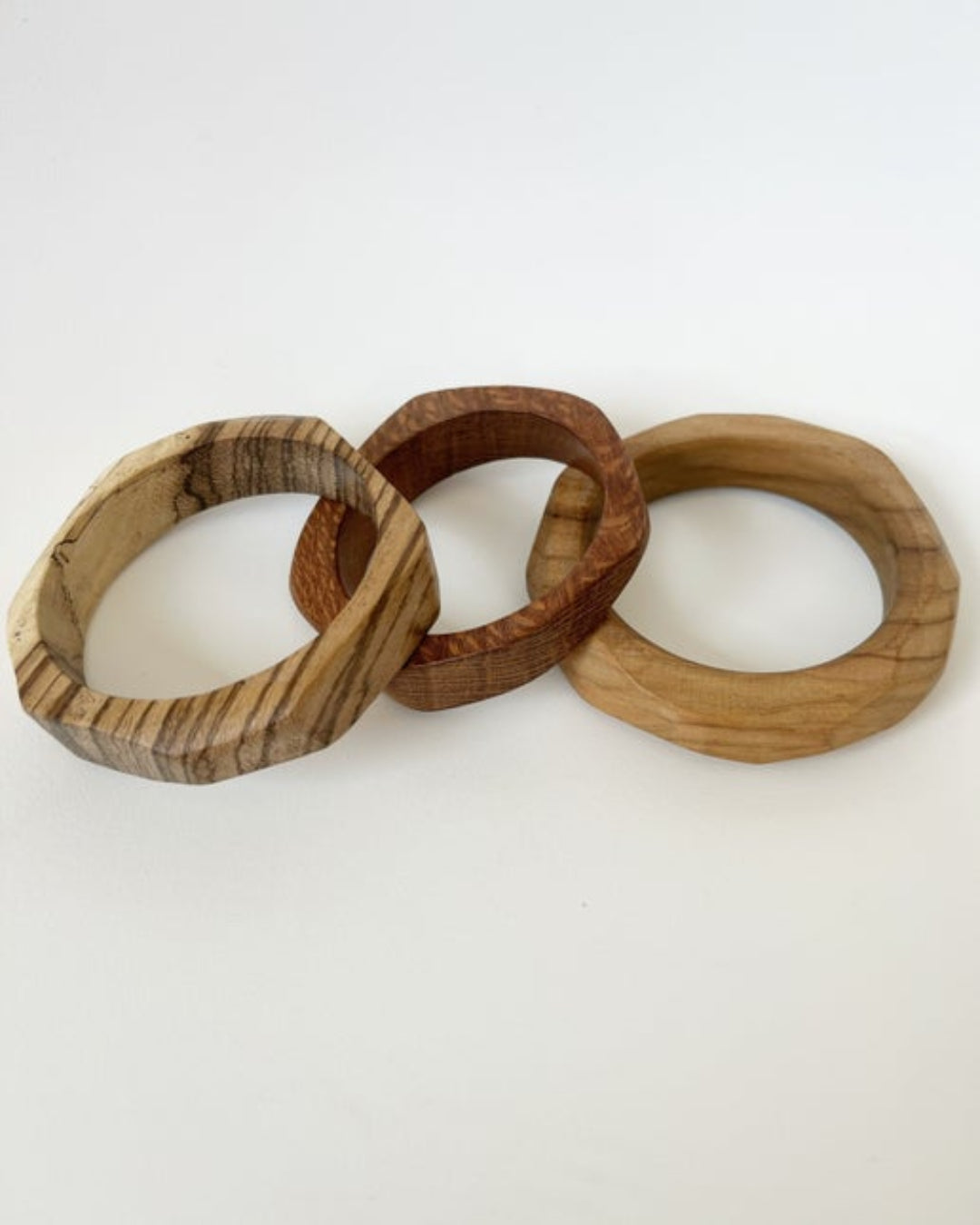 Three wooden bracelets of different designs on a white background