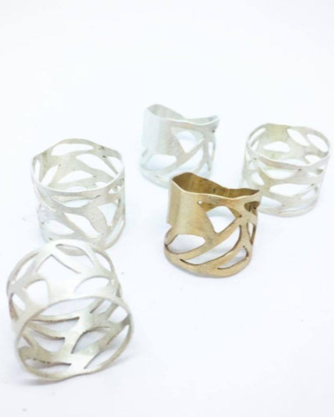 Collection of four silver rings and one bronze ring with intricate design on a white background 
