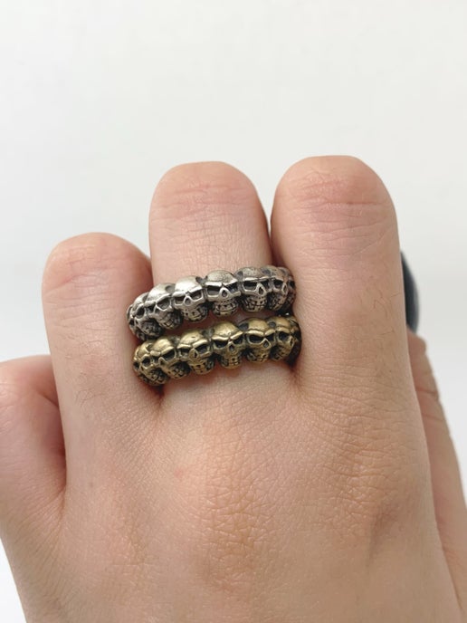 Two skull-themed rings, one silver and one bronze, on a finger against a white background