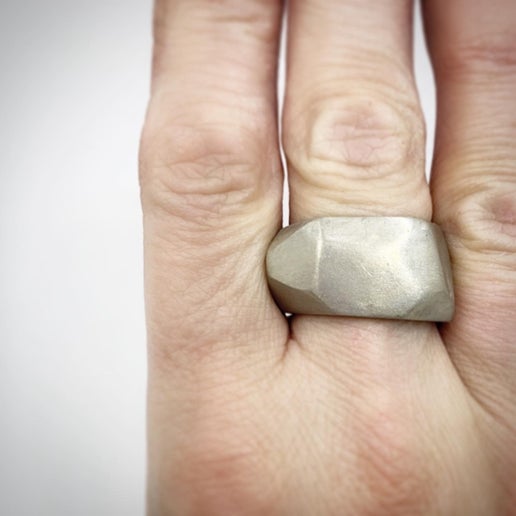 Hand wearing a textured silver ring on a plain background