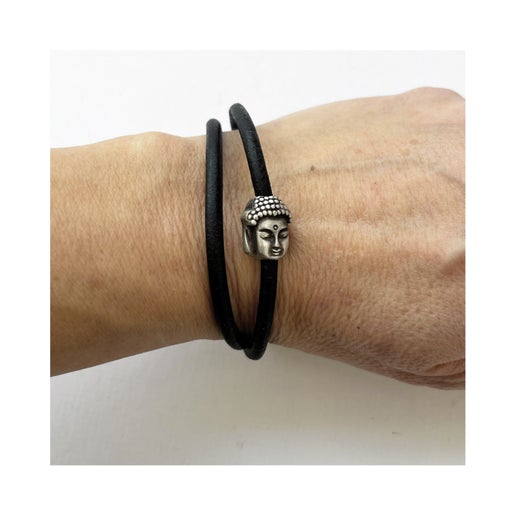 Black leather bracelet with Buddha head charm on a wrist against a white background