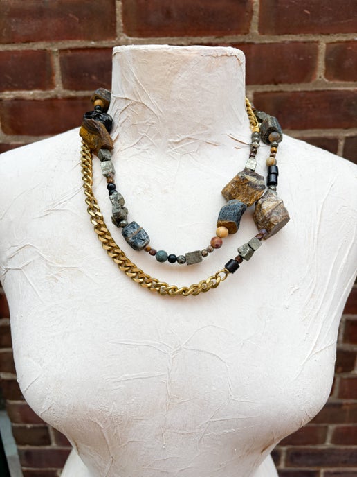 Necklace with stone beads and gold chain on a mannequin bust against a brick wall.