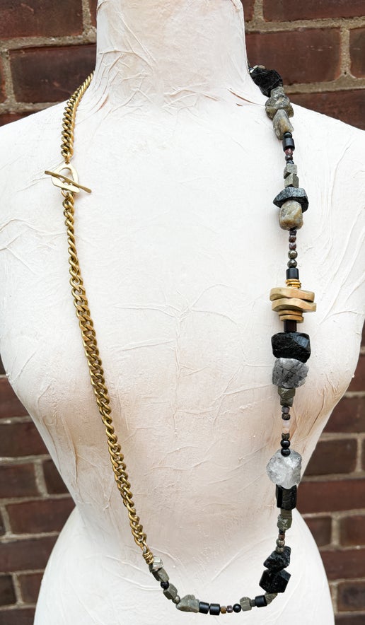 Gold necklace with stone beads displayed on a mannequin against a brick wall