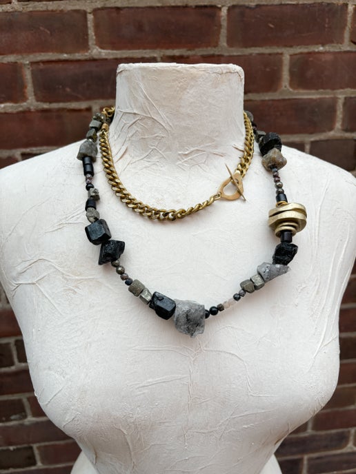 Necklace with black and gray beads and gold accents on a mannequin bust against a brick wall.